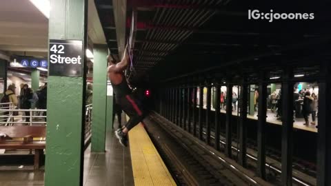 Pt. 2 guy wearing headphones and tank top works out in subway station pull ups