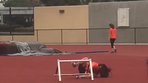 Orange shirt girl jumps hurdle on red track and falls down