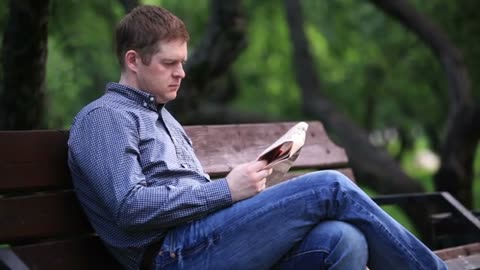 Man reads a newspaper on a bench in the park