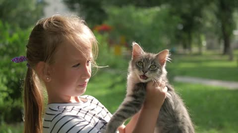 Cute little child blond girl with kitten, girl playing with cat in the summer park