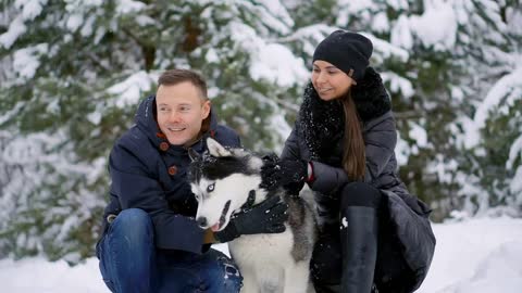 Family portrait of cute happy couple hugging with their alaskan malamute dog licking man's face