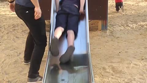 Little kid with hat gets pulled down metal slide hits chin at bottom