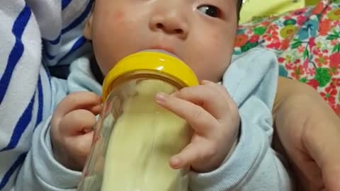 This is a video of a baby holding a bottle and drinking formula,