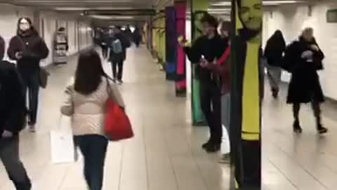 Subway musician plays guitar and sings, two guys bow their heads up and down the to beat