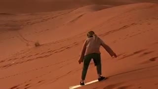 Guy rides white snowboard down sand dune and falls down