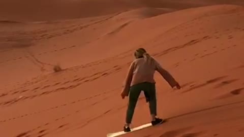 Guy rides white snowboard down sand dune and falls down