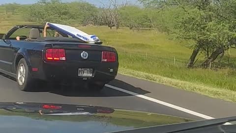 Guy in black car holding surfboard over his head