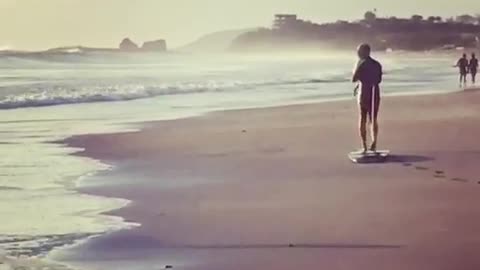 Man in black dragging surfboard on beach