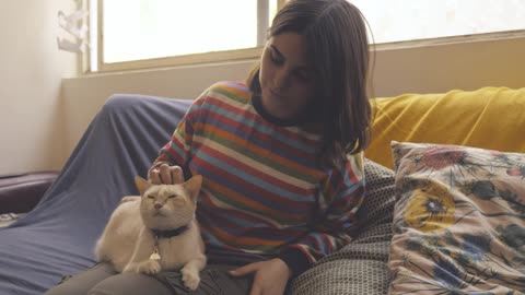 A woman sits on a couch and pets a cat