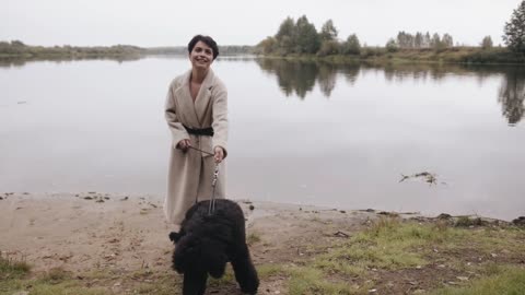 An exquisite young woman with short hair walks along the river bank with a poodle