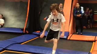 Boy in grey shirt does flip on orange trampoline, falls on head