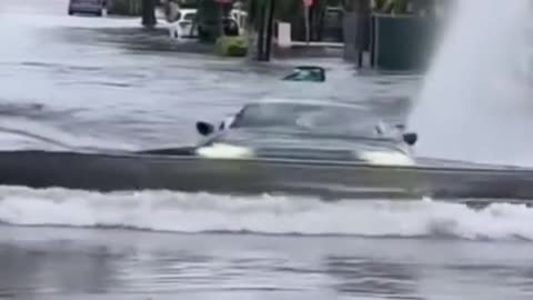 The car is driving across the stagnant water road.