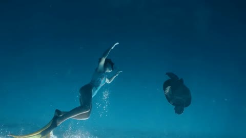 Girl in swimsuit, mask and fins swimming freely underwater with wild turtle