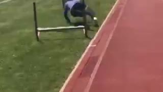 Blue shirt girl tries to jump hurdle on grass near track