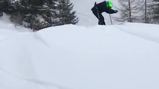 Kid in green helmet skis down hill and faceplants in the snow