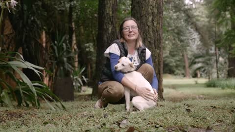 Portrait of an attractive happy woman kneeling on the ground petting her dog in slow motion