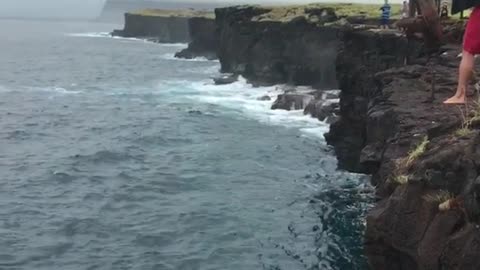 Shirtless man backflipping off ladder on cliff flops
