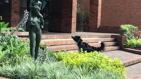 Black dog barks at statue of lady carrying little boy