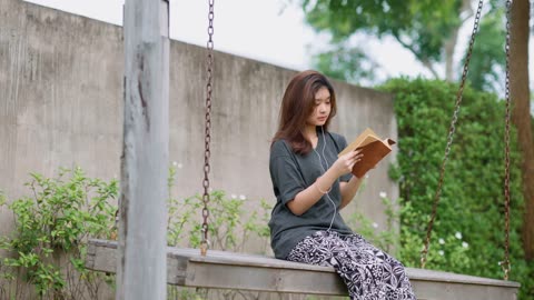 "A Teenage Asian Girl Reads a Book While Sitting on a Swing"