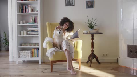 A Woman Having Coffee And Reading Magazine While Seated On A Chair With Her Dog