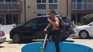 Guy on electric scooter carrying blue surf board