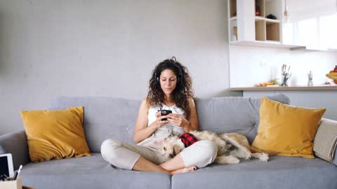 Relaxed woman with two pet dogs sitting indoors at home, listening to music