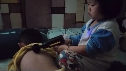 Adorable 3-year-old girl massaging her elder brother