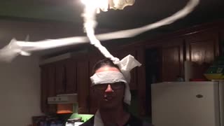 Guy in kitchen has toilet paper on head and ceiling fan