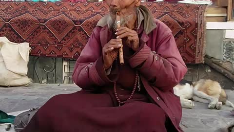 A tribal man in traditional attire playing flute in Leh Market, Leh, Jammu and Kashmir, India