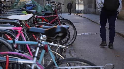 Handheld Shot of Bicycles Locked to Racks as Pedestrians Walk Past