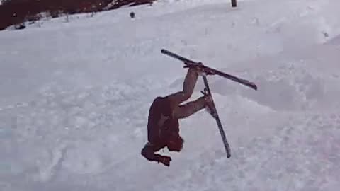 Guy in grey ski pants tries front flip on skis and falls in snow