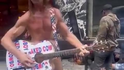 New York's famous 'Naked Cowboy' singing in front of migrants overflowing the streets of Manhattan..