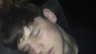 Guy puts cigarette in mouth of sleeping friend