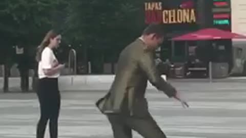 Guy in suit tries to ride skateboard and falls onto pavement