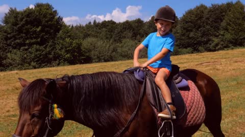 Happy boy in helmet riding brown horse in mountains