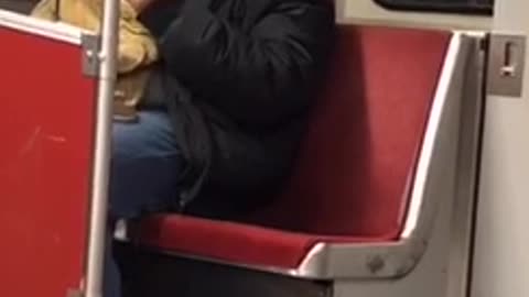 Guy wearing earphones headbangs to music on subway train