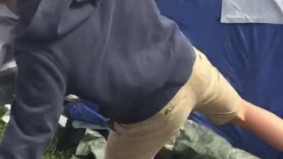 Guy in khaki shorts and blue sweater trips over tent