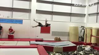 Guy in gymnasium back flips lands on grey mat