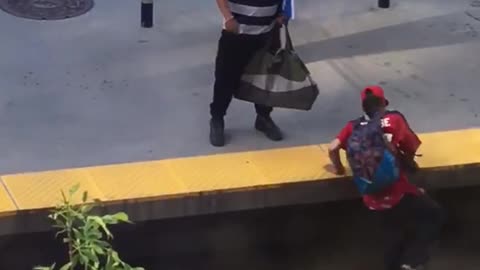 Guy in red falls asleep while standing at train station and falls onto tracks striped shirt guy tries to help him