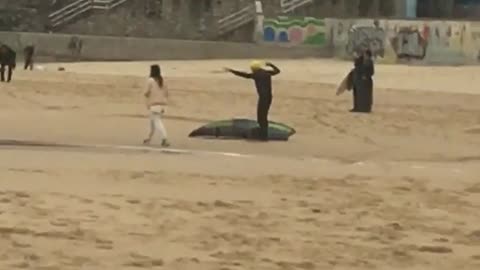 Old guy on sand pretending to paddle and swim in wet suit