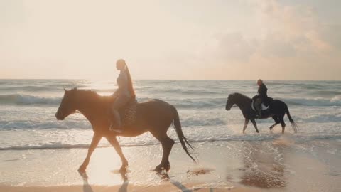 View of women riding beautiful horses wading through the sea splashing water