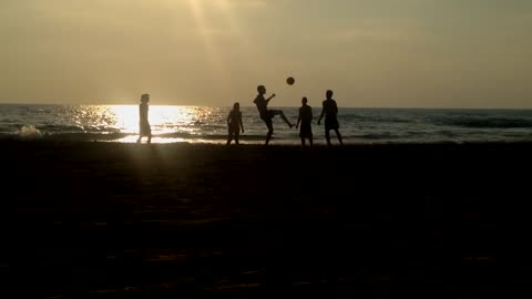 Guys And Girls On Beach Kick Volleyball Around