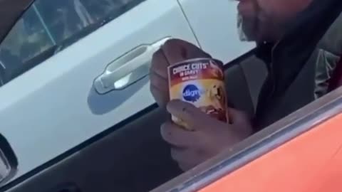 Man is driving car eating a can of dog food