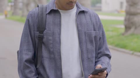 Tracking Shot of Young Man Walking Whilst Looking at Smartphone