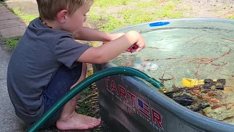 Theo playing and learning about currents in the trough with a sprinkler and rescue vehicles!