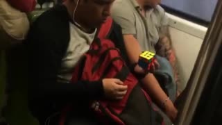 Man solves rubix cube with one hand on subway