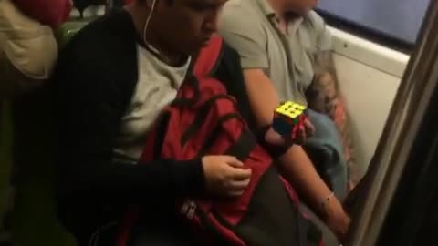 Man solves rubix cube with one hand on subway