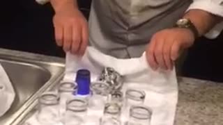 Guy in white shirt tries to pull kitchen towel from under glasses. breaks all of them