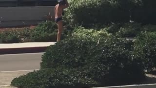 Guy in speedo carries surfboard on his head while barefoot