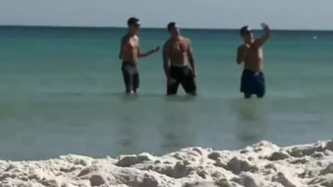 Three shirtless dudes trying to take selfie in water beach